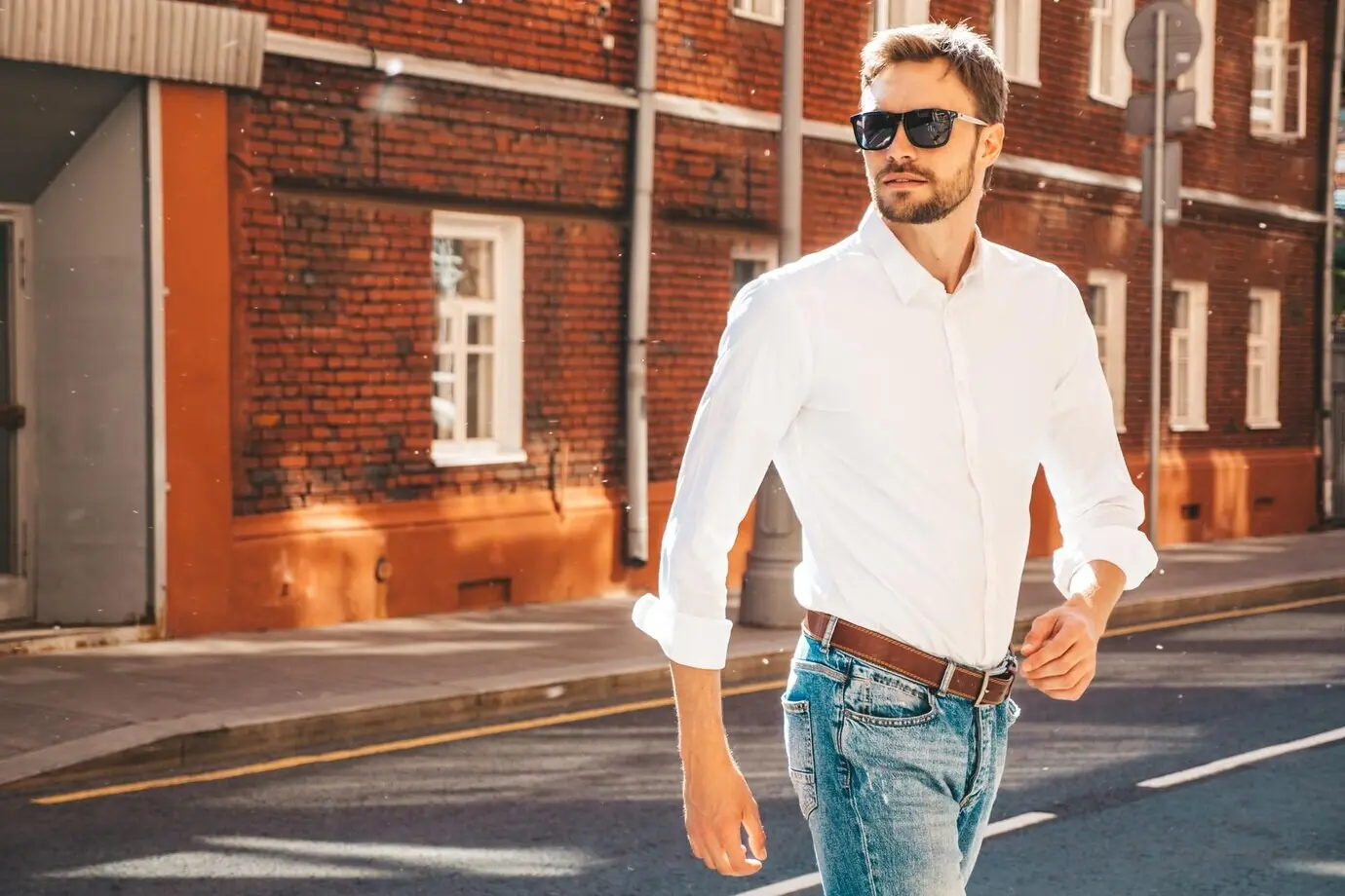 Porträt eines gutaussehenden, selbstbewussten, stylischen Hipster-Lumbersexual-Models. Moderner Mann in weißem Hemd. Modebewusster Mann posiert mit Sonnenbrille vor Straßenkulisse, im Freien bei Sonnenuntergang.